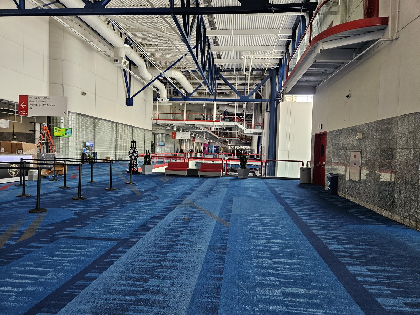 An empty convention center concourse before opening, overhead signage directing to meeting rooms 320 through 382, sunlight across the floor.