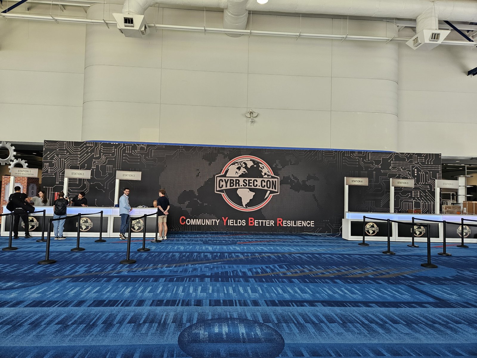 A conference registration wall with six staffed check-in stations and a handful of early attendees collecting badges.