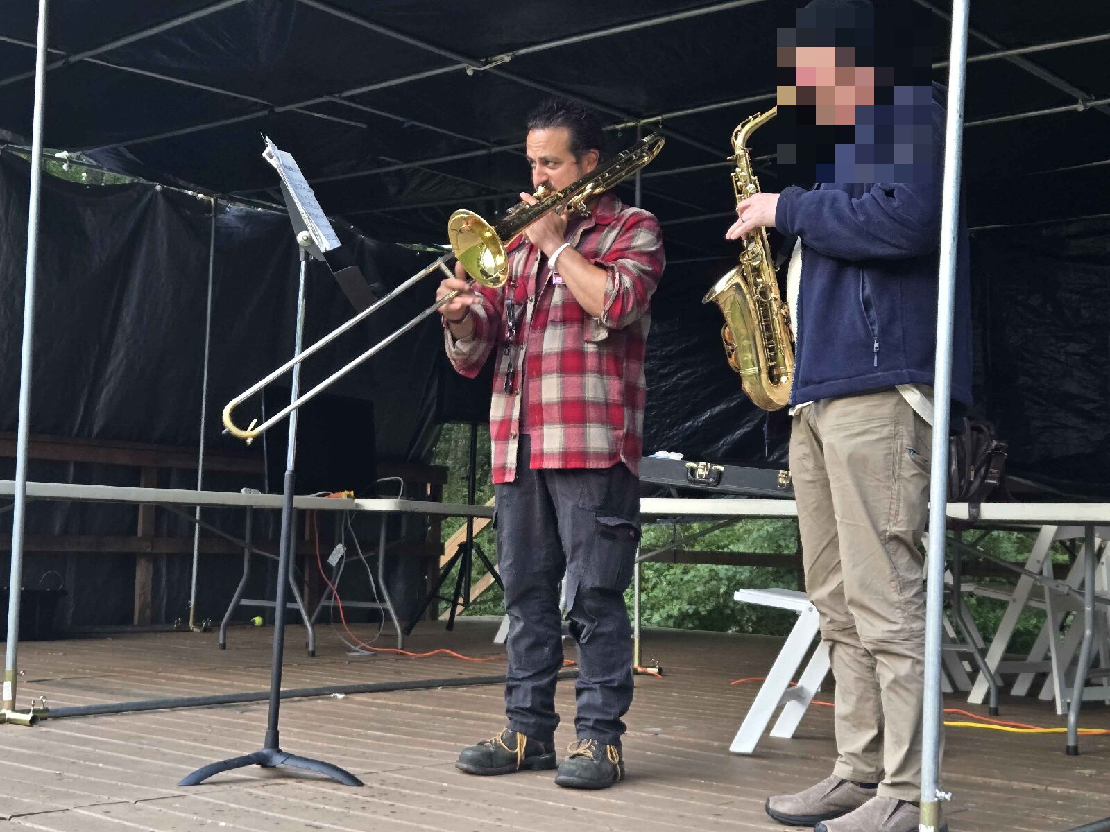 The author playing trombone beside a saxophone player under the stage tent at the jazz jam.